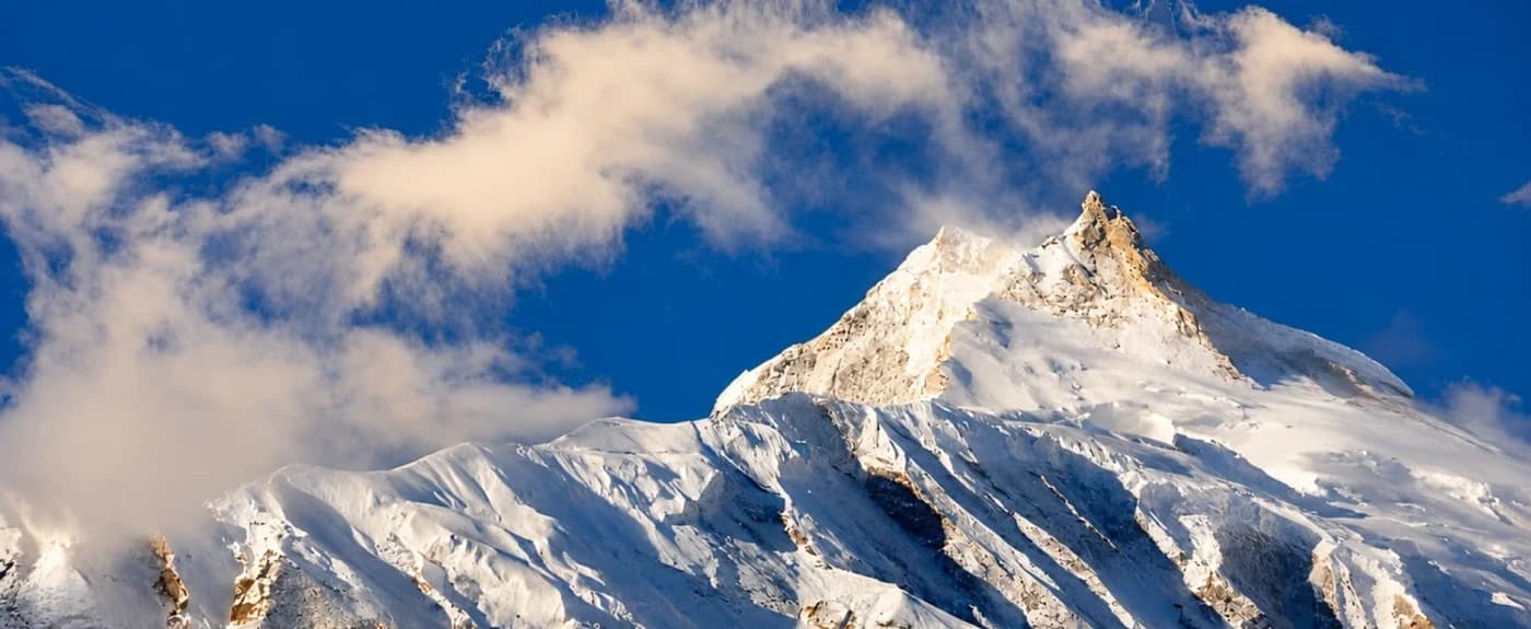 Snow-covered Manaslu Mountain in Nepal Himalaya illustrating the best time for Manaslu Circuit Trek, with clear blue skies and clouds, Thrill Himalaya Treks